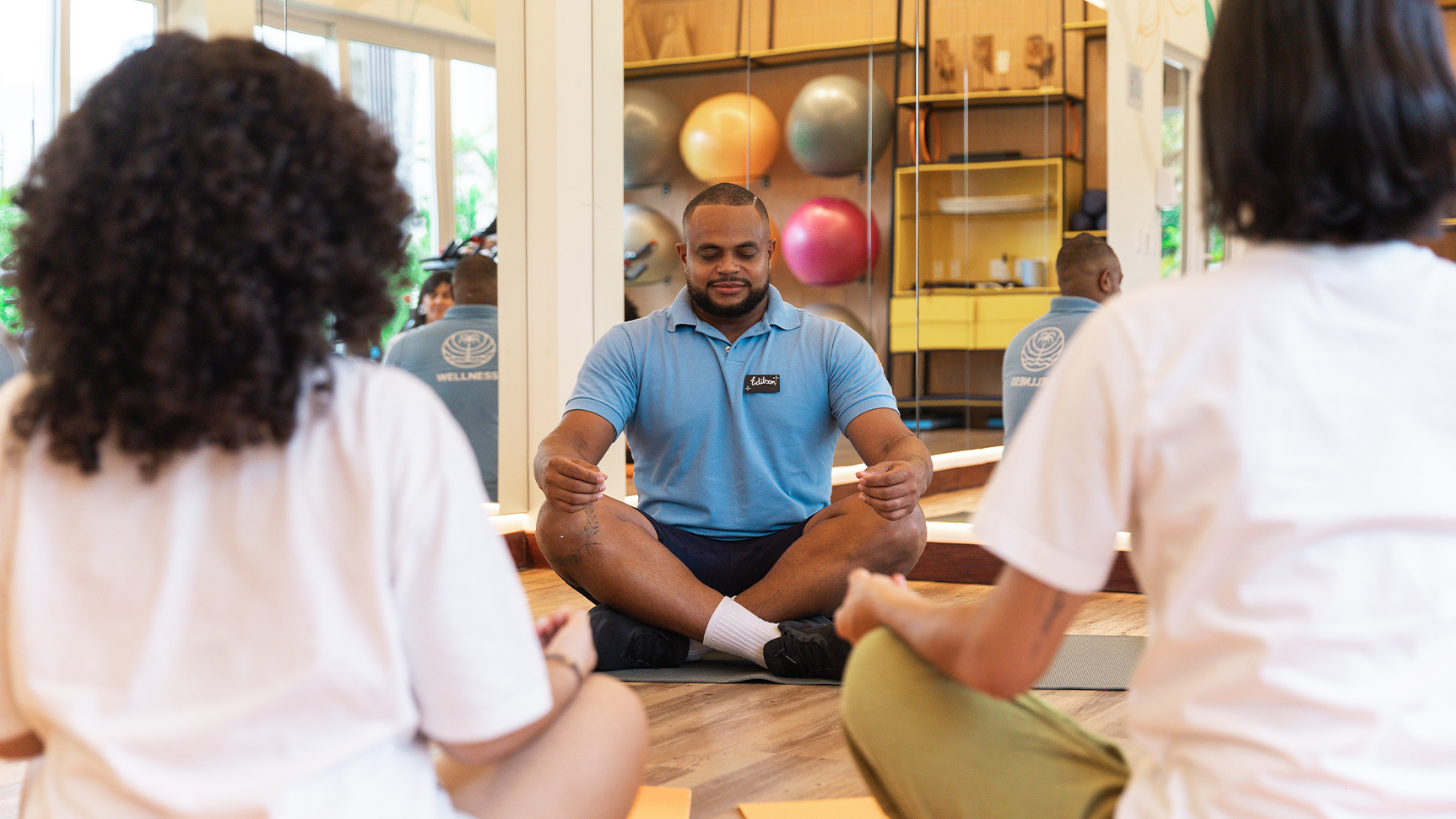 Colaborador de Wellness do Japaratinga Lounge Resort ensinando prática de meditação pra hóspedes em sala de multiuso. 