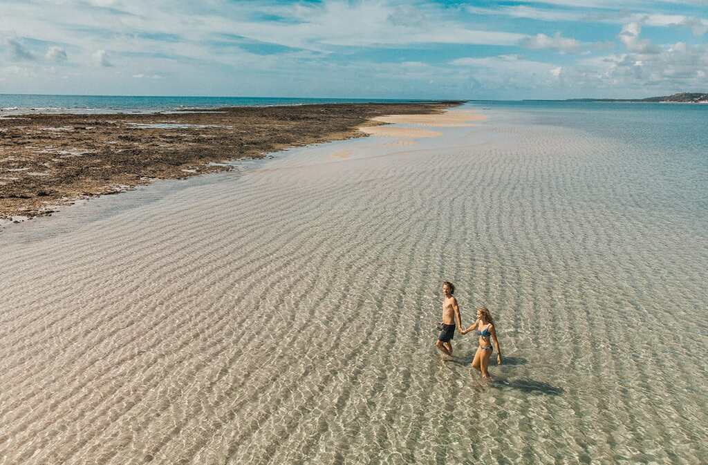 Casal caminhando de mãos dadas nas águas cristalinas de Japaratinga, destino paradisíaco incluso na Black Friday Amarante.