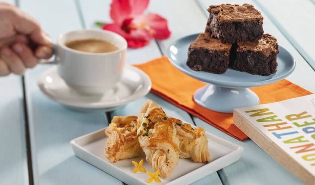 Mesa com café, brownies de chocolate e croissant em ambiente aconchegante, ideal para café da manhã ou lanche da tarde.