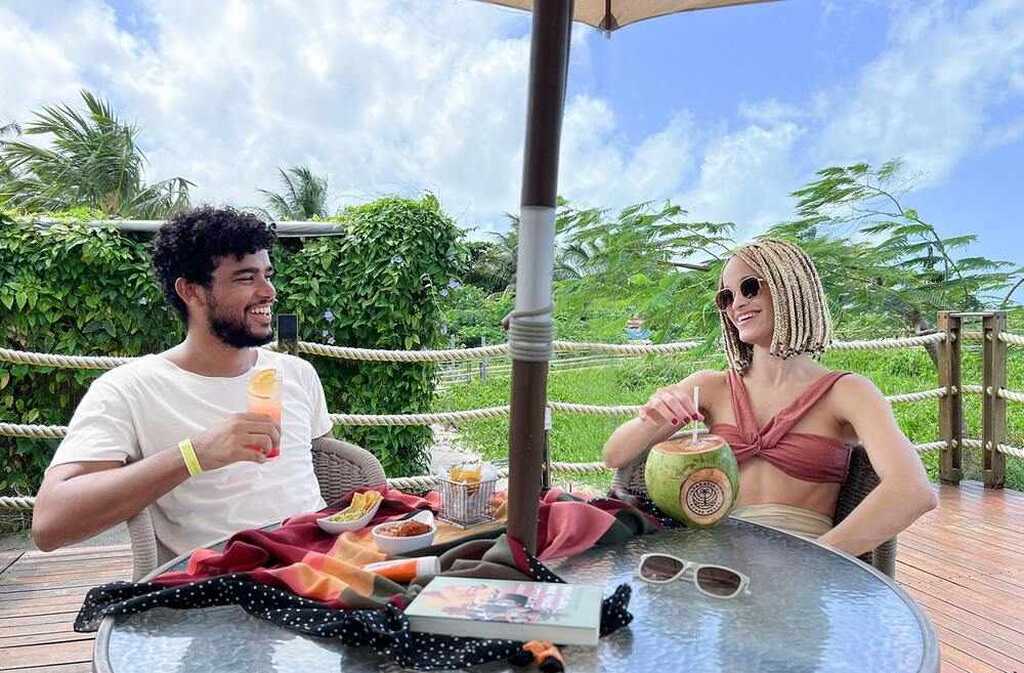 Homem e mulher relaxando e tomando drinks ao ar livre no Resort Japaratinga All Inclusive com vegetação ao fundo.