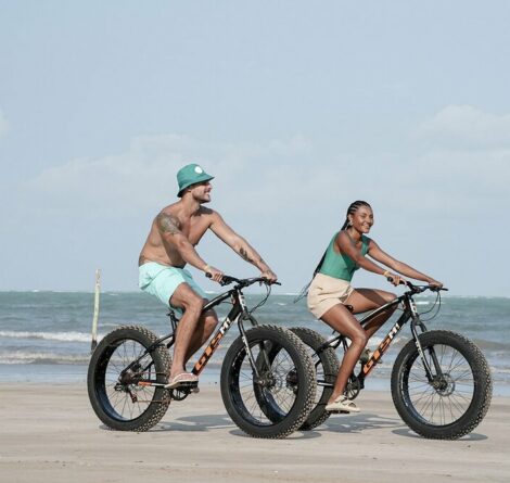 pessoas andando de bicicleta em praia, ilustrando a prática de turismo sustentável
