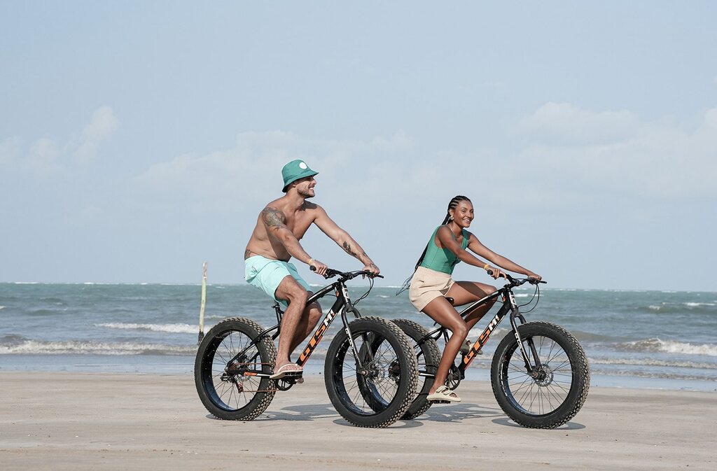 pessoas andando de bicicleta em praia, ilustrando a prática de turismo sustentável
