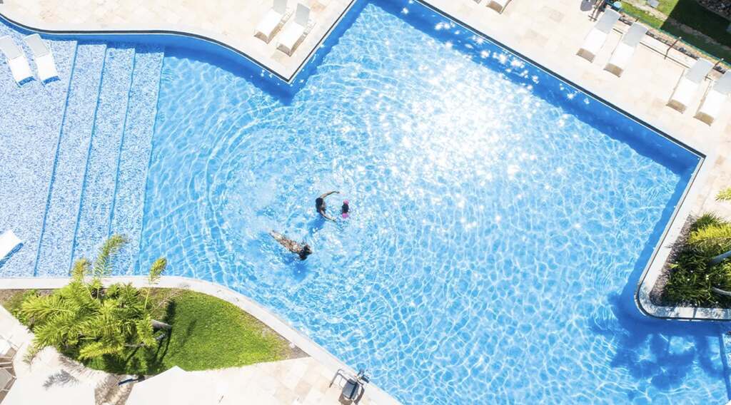 Piscina azul cintilante em resort com piscina aquecida, vista de cima, com hóspedes nadando e relaxando sob o sol.