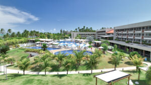Vista aérea do Japaratinga Lounge Resort à beira-mar, com piscinas amplas e quadras, cercado por vegetação e coqueiros.