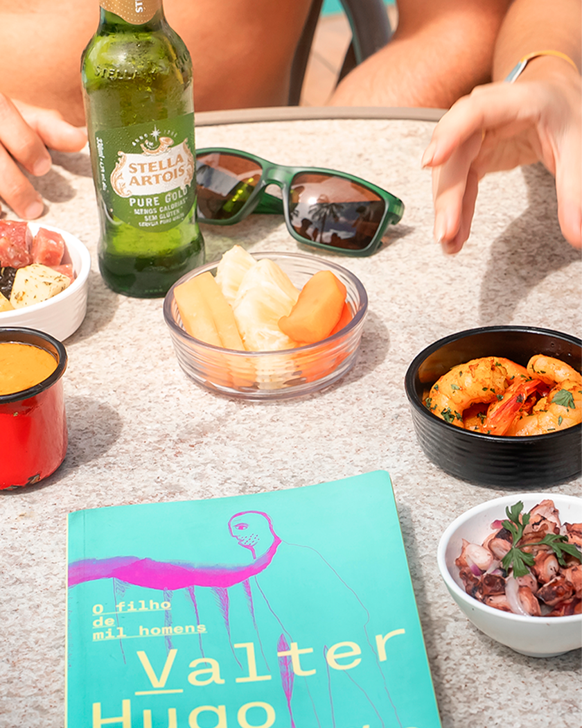 Gastronomia All Inclusive Premium Mesa do All Inclusive Premium com pratos e petiscos, queijos, camarões hamburguer e bebidas como Cerveja Stella Artois e drink servidos com casal na mesa.