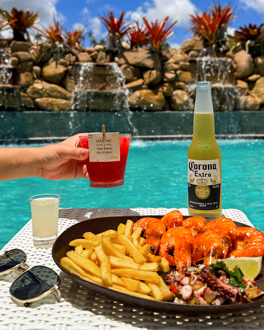 Sabor de férias é imperdível Petiscos e bebidas servidos na piscina do Salinas Maragogi All Inclusive. Com pequenas cachoeiras caindo na piscina com pedras e plantas.