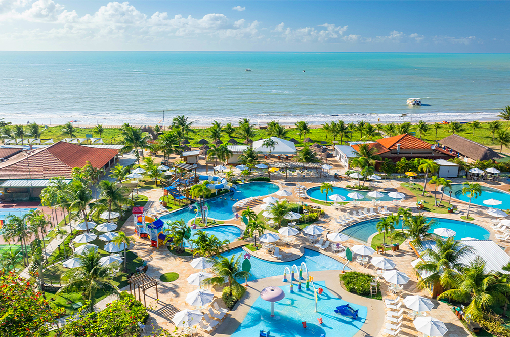 Estrutura completa pra todas as idades Vista aérea do Salinas Maceió à beira mar. É possível ver as piscinas ao centro e nas laterais das estruturas do resort, ao fundo a imensidão da praia de Ipioca e o céu sem nuvens.