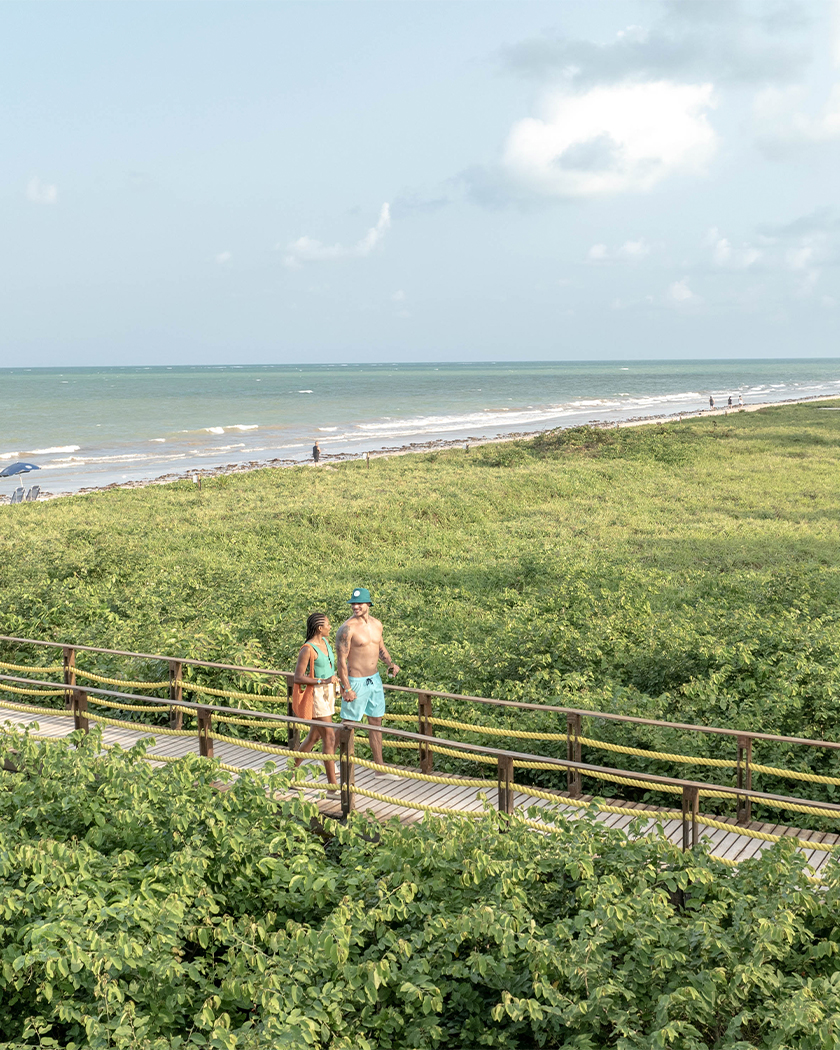 resort na praia Casal atravessando a ponte de madeira por cima de área preservada na praia de Japaratinga, há uma grande faixa de vegetação com coqueiros ao longo da praia.