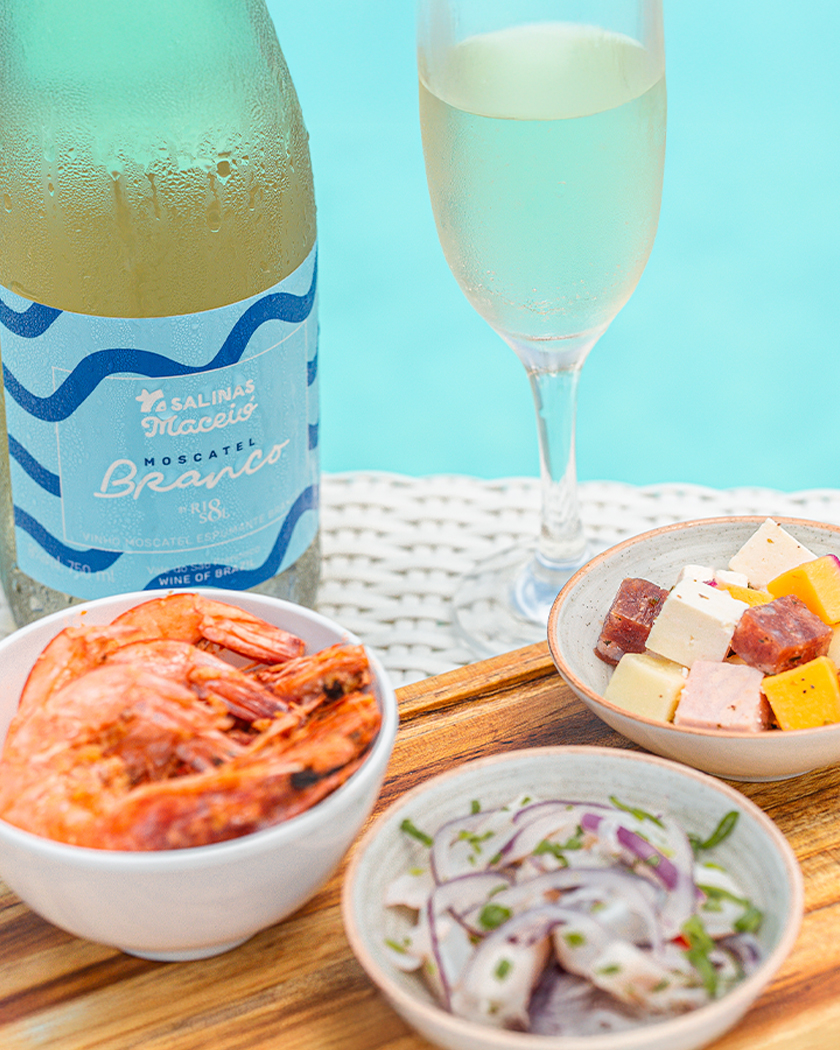 destinos paradisíacos Diversos petiscos camarão, ceviche e queijos sobre uma tábua de madeira em cima de uma mesa branca, do espumante Moscatel Branco na beira da piscina do Salinas Maceió.