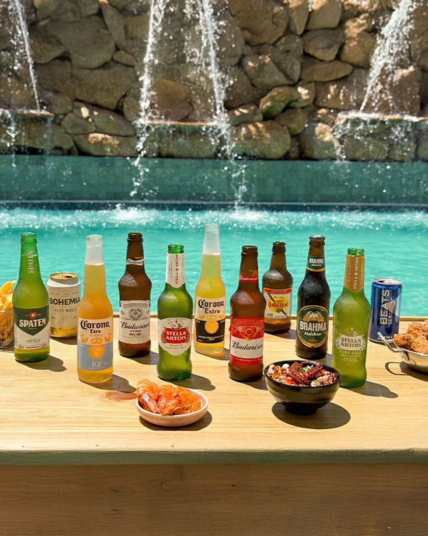all inclusive 24h por dia Mix de cervejas latas e long neck, com petiscos ao redor, e ao fundo a piscina do Salinas Maragogi com cascata.