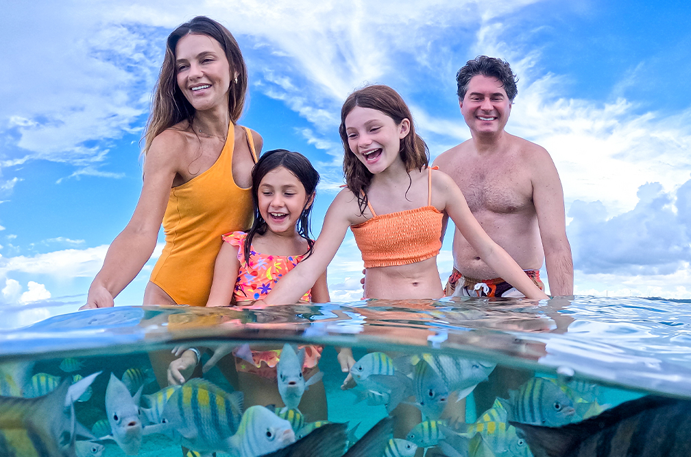 Contato com a natureza inesquecível em Galés de Maragogi Família em foto meio subaquática. Pai, mãe e duas filhas, com peixinhos listados ao redor deles.