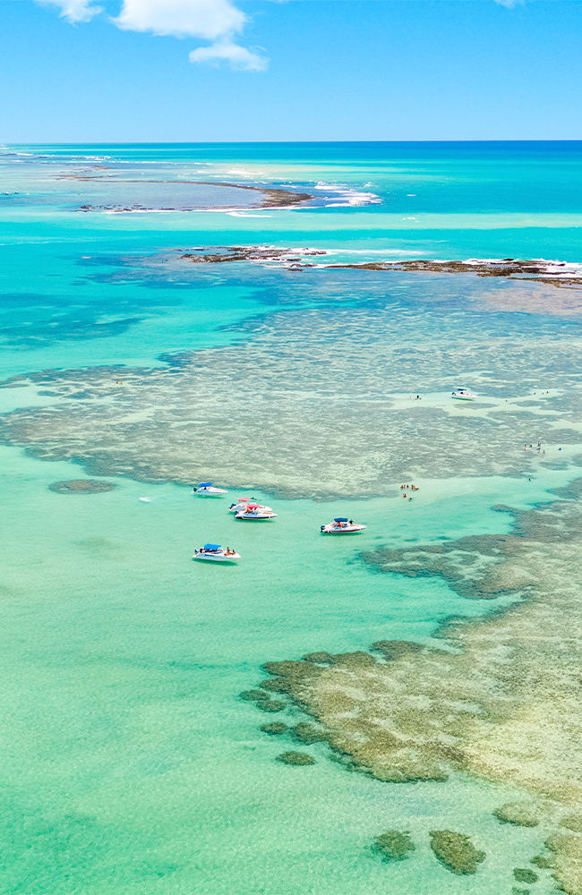 Piscinas naturais de Barra Grande que se transforma em cartão-postal Vista aérea das piscinas naturais de Barra Grande, com águas cristalinas e formações de corais, barcos ancorados e turistas desfrutando do mar em cenário paradisíaco.